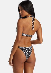 Zwart-wit gestippelde bikini met een halternek en striksluiting. Heeft een lage taille en een gestructureerd stofontwerp.