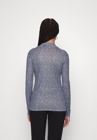 Blusa a maniche lunghe, di colore blu scuro, con un motivo floreale in blu e bianco. Tessuto leggero e trasparente, con colletto alto e design aderente.