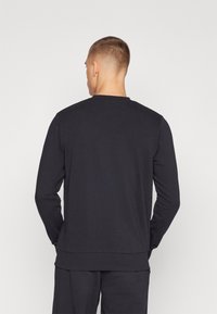 Czarny długi rękaw sweatshirt z okrągłym dekoltem i luźnym krojem. Wykonany z miękkiego materiału bawełnianego, z prążkowanymi mankietami i dołem.