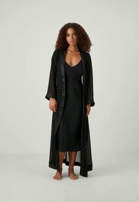 Crna, prozirna kimono haljina s dugim rukavima preko uske crne haljine. Glatka tkanina s satenskim obrubima duž rubova.