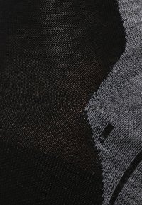 Tela en negro y gris con un patrón texturizado. Presenta hilos finos y tejidos, así como una área sólida en contraste. Material suave y elástico.