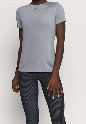 Person iført en tætsiddende lysegrå Nike t-shirt med korte ærmer og sorte teksturerede leggings, stående mod en ensfarvet baggrund.