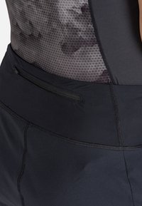 Pantaloni corti sportivi neri con un pannello testurizzato grigio scuro, una tasca con zip in vita e cuciture flatlock per un comfort migliorato.