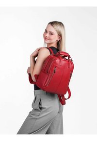Červený kožený batoh s více kapsami na zip, strukturovaným tvarem a dvojími možnostmi nošení (horní ucho a ramenní popruhy).