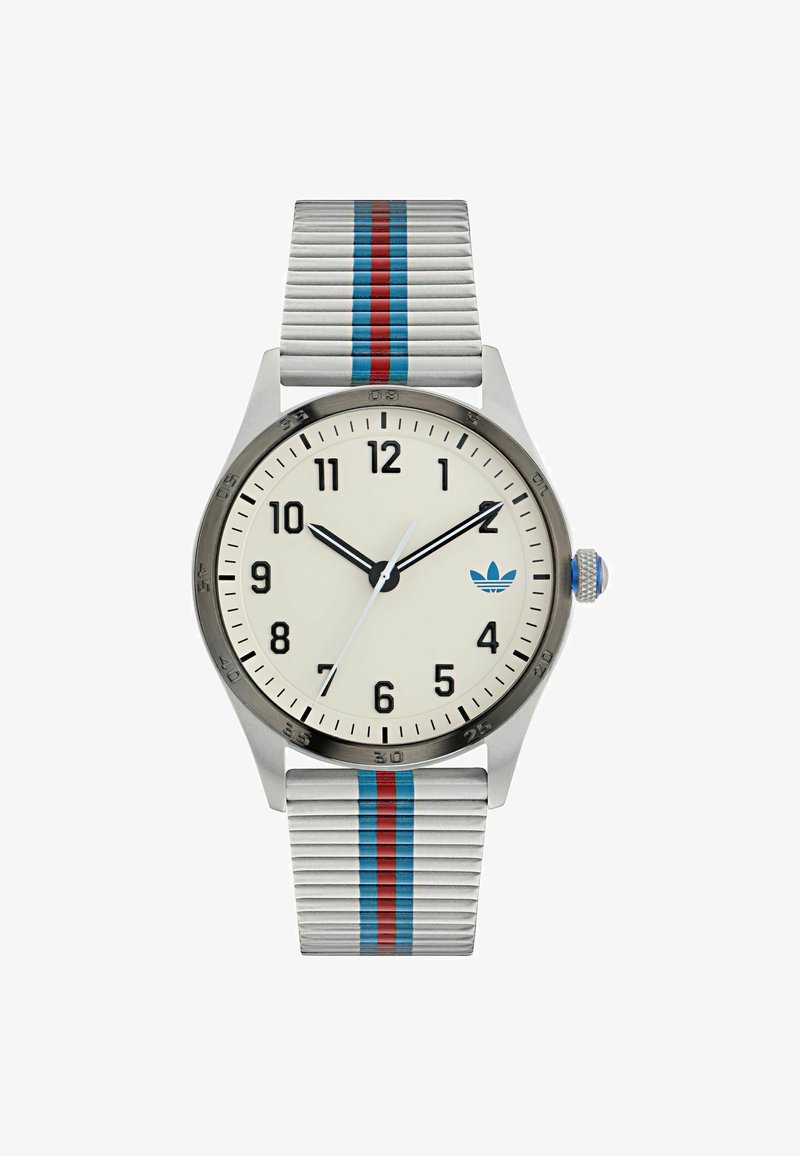 Ezüst analóg óra fehér számlappal, fekete órajelzőkkel és kék logóval. Csíkos ezüst pánttal rendelkezik, piros és kék kiegészítőkkel.