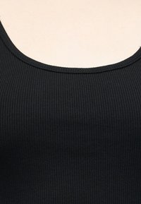 Gros plan sur un tissu noir côtelé avec un bord d'encolure arrondi sur un fond de peau claire.