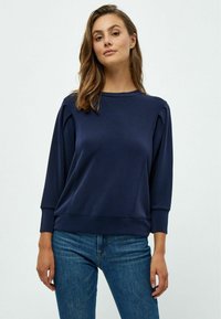 Sudadera azul marino con mangas largas, cuello redondo y puños de canalé. Presenta pliegues sutiles en los hombros y una textura de tela suave.
