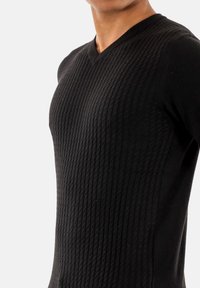 Maglione nero con scollo a V e un motivo ribattuto a trama. Presenta una forma aderente e un tessuto liscio, che mette in risalto il design lavorato a maglia.