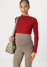 Rode geribbelde lange mouwen top, gecombineerd met beige hoge taille leggings. Model houdt een kleine olijfgroene handtas vast. Eenvoudig ontwerp en zachte texturen.