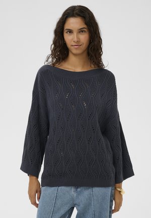 Marineblauer Strickpullover mit wellenförmigem Muster, weitem Ausschnitt und dreiviertellangen Ärmeln, kombiniert mit hellblauen Jeans.