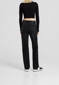 Black jeans with a straight-fit design, five pockets, and a slightly worn texture, paired with white sneakers. Back view showcased.