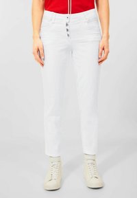Los vaqueros de denim blancos tienen un ajuste slim con una cintura de altura media, cinco bolsillos y un cierre de botón con cuatro botones. Combinados con zapatillas blancas.