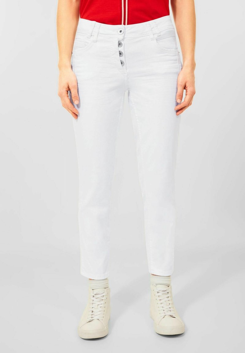 Los vaqueros de denim blancos tienen un ajuste slim con una cintura de altura media, cinco bolsillos y un cierre de botón con cuatro botones. Combinados con zapatillas blancas.
