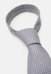 Corbata gris con un patrón y textura tejida. El diseño presenta una serie de pequeñas formas geométricas en diferentes tonos de gris.