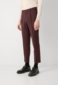 Maroon tailored trousers with a pleated front, cropped length, and cuffed hems, paired with black lace-up shoes and dark socks.