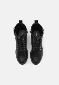 Botas de cuero negro hasta el tobillo con punta redonda, cordones en la parte delantera y detalles en hardware plateado. Cuenta con una lengüeta en la parte posterior para facilitar su uso.