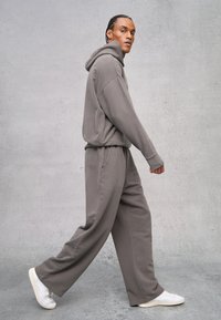 Grauer Kapuzenpullover mit passenden weiten Hosen, gefertigt aus weichem Stoff. Bietet einen lässigen Schnitt und eine Kängurutasche. Kombiniert mit weißen Sneakers.