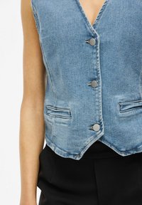 Denim prsluk u svijetloplavoj boji s dubokim V-izrezom, pet sivih dugmadi i dva bočna džepa; ima uski kroj išiljenu siluetu.
