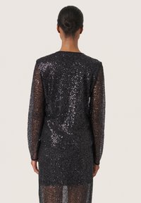 Abito nero di paillettes con maniche lunghe, tessuto trasparente e taglio dritto. Caratterizzato da un colletto rotondo e schiena coperta.