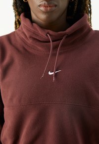 Bordeauxfarbener Fleece-Sweatshirt mit hohem Kragen, Kordelzügen und kleinem weißen Nike-Logo auf der Brust. Weiche Textur und bequeme Passform.
