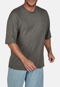 T-shirt in cotone verde oliva con maniche corte, scollo rotondo e fessure laterali, caratterizzato da una finitura leggermente testurizzata.