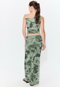 Grön blommönstrad tvådelad outfit bestående av en off-shoulder topp och en figurnära maxikjol, tillverkad av lätt, svävande tyg.