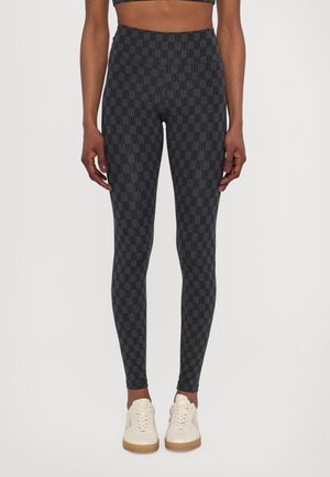 Hoge zwarte legging met een algehele gepatternde logoprint. Zachte, rekbare stof met een gladde textuur. Gemaakt met lichtgekleurde sneakers.