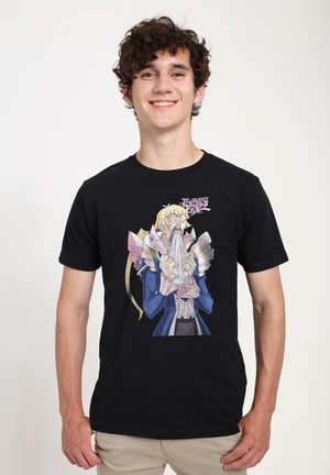 Junger Mann lächelt, trägt ein schwarzes T-Shirt mit einem schockierten Anime-Charakter aus Yu-Gi-Oh! GX, der Papiere vor den Mund hält.