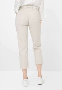 Beige cropped Hose mit einem strukturierten Muster, ausgestattet mit zwei Gesäßtaschen und einem Gürtel. Kombiniert mit weißen Sneakers für einen lässigen Look.