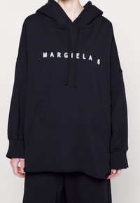 Felpa nera oversize in morbido tessuto, con tasca frontale, cappuccio con cordino e logo ricamato bianco "MARGIELA 6".