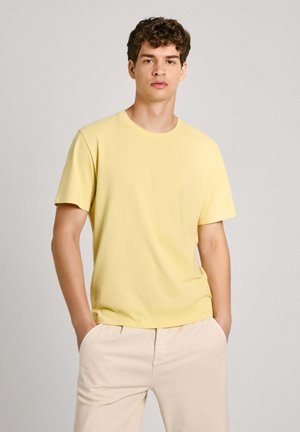 Geel katoenen T-shirt met een ronde hals en korte mouwen, met een klein logo op de linkerkant van de borst. Gekleed met lichtbeige broek.