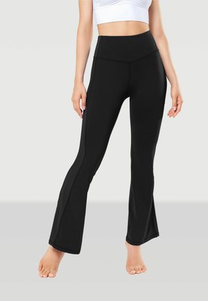 Black flared leggings made of stretchy material with a high waistband. Features include side seams and a smooth texture. Barefoot model.