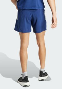 Námornícke športové šortky s hladkou textúrou, elastickým pásom a tromi vertikálnymi bielymi pruhmi na každej strane, spárované s čiernymi topánkami.