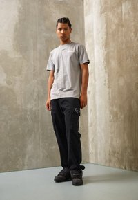 Gray short-sleeved t-shirt with logo on chest, paired with black cargo pants featuring pockets and decorative stitching, and black sneakers.