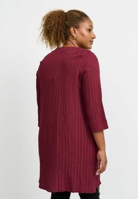Burgundiklänning med en texturerad, vertikalt randig design, trekvartsärmar och rund halsringning, som når mitt på låret, utan synliga knäppningar.