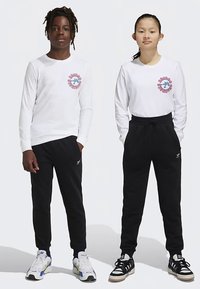 White long-sleeve shirts with logo prints, paired with black sweatpants. The boy wears colorful sneakers; the girl wears black and white sneakers.