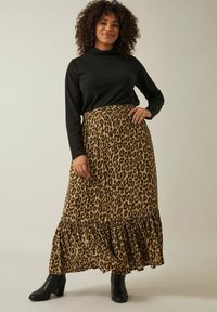 Top negro de manga larga combinado con una falda maxi de estampado de leopardo con volantes en el dobladillo. La modelo lleva botas de tobillo negras con tacón cuadrado.