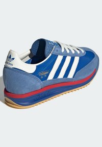 Modré semišové tenisky s bílými pruhy, gumovou podrážkou, červenou mezipodešví a zlatým logem "adidas SL 72". Mají texturovaný jazyk a tkaničky.