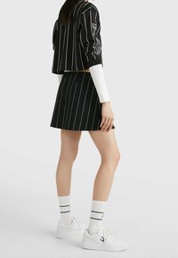 Zwart gestreepte crop sweatshirt met lange mouwen, gecombineerd met een zwarte geplooide rok. Witte sokken en sneakers maken de look af.