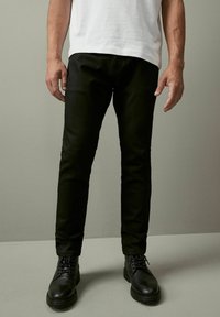 Mustat slim-fit-housut, jotka on valmistettu kestävästä kankaasta, jossa on sileä pinta ja minimaalinen yksityiskohta. Yhdistetty mustiin nauhakenkäisiin.