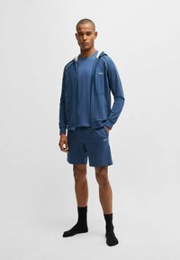 Blue athletic ensemble featuring a zip-up hooded jacket, short sleeves, matching shorts, and black socks. The fabric appears smooth and lightweight.