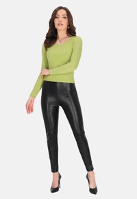 Grünes gestreiftes Langarmoberteil mit Rundhalsausschnitt, kombiniert mit hoch geschnittenen schwarzen Leggings aus Kunstleder und schwarzen High-Heels.