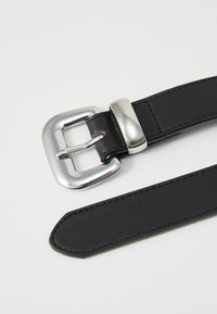 Cinturón de cuero negro con hebilla metálica plateada, con forma rectangular y textura suave, que presenta detalles de costura sutiles.