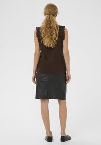 Braunes ärmelloses Oberteil mit Rüschenkanten, kombiniert mit einem schwarzen Lederrock in knielanger Länge. Das Outfit hat eine einfache, glatte Textur und Passform.