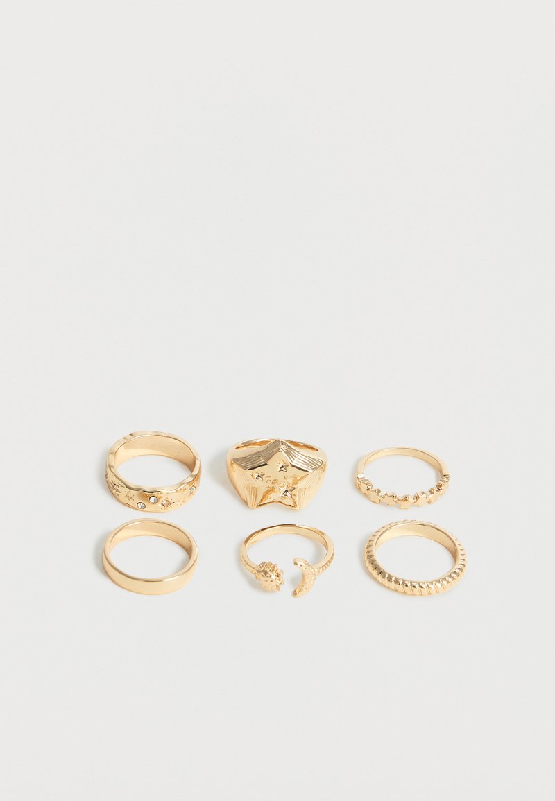 Έξι χρυσά δαχτυλίδια με διάφορα σχέδια, συμπεριλαμβανομένων αστεριών, πολύτιμων λίθων, λείων στεφανιών και υφασμένων μοτίβων, τοποθετημένα σε δύο σειρές πάνω σε λευκό φόντο.