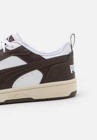Brune og hvite sneakers med en glatt lær overdel, teksturerte detaljer, snøring og en beige gummisåle med merke detalj.