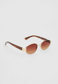 Lunettes de soleil écaille de tortue avec des verres ovales, des accents en métal doré et une teinte marron dégradée. Montures fines avec un motif, finition brillante.