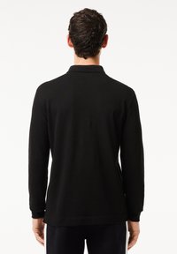 Schwarzes Polohemd mit langen Ärmeln und Kragen, gefertigt aus einem glatten Stoff. Verfügt über gerippte Bündchen und einen geraden Saum.