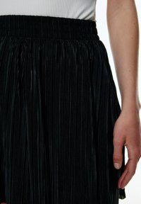Zwarte geplooide rok met een gestructureerd oppervlak en een elastische tailleband, met verticale lijnen en een soepele afwerking langs de zoom.