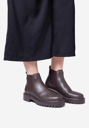 Brown leather ankle boots with elastic side panels, rubber soles, and a textured finish. Designed with a rounded toe and subtle logo detail.